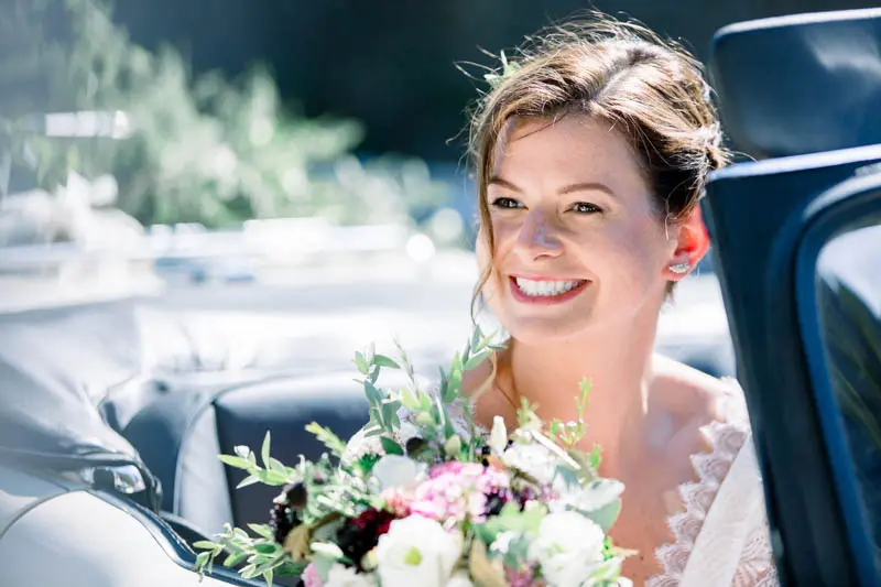 The radiant bride holding her bouquet in a vintage convertible car