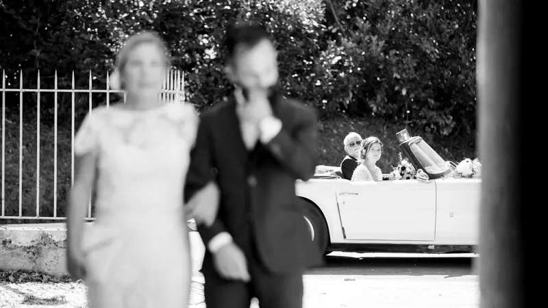 The newlyweds by a vintage car after the ceremony, in black and white