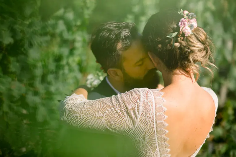 The bride and groom embracing among the greenery, flowers in the bride's hair
