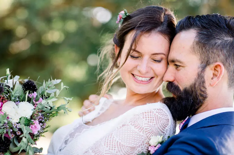 Tender portrait of the couple cheek to cheek, bouquet in hand