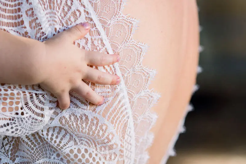 A baby's hand resting on the lace back of the bride's gown