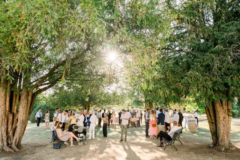 Guests gathered in the shade of tall trees for the cocktail hour at Château de Seguin