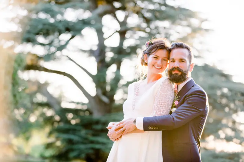 The bride and groom embracing beneath a great cedar in the château grounds