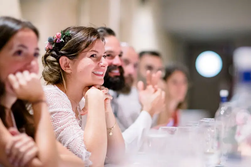 The bride and guests smiling as they listen to speeches at dinner