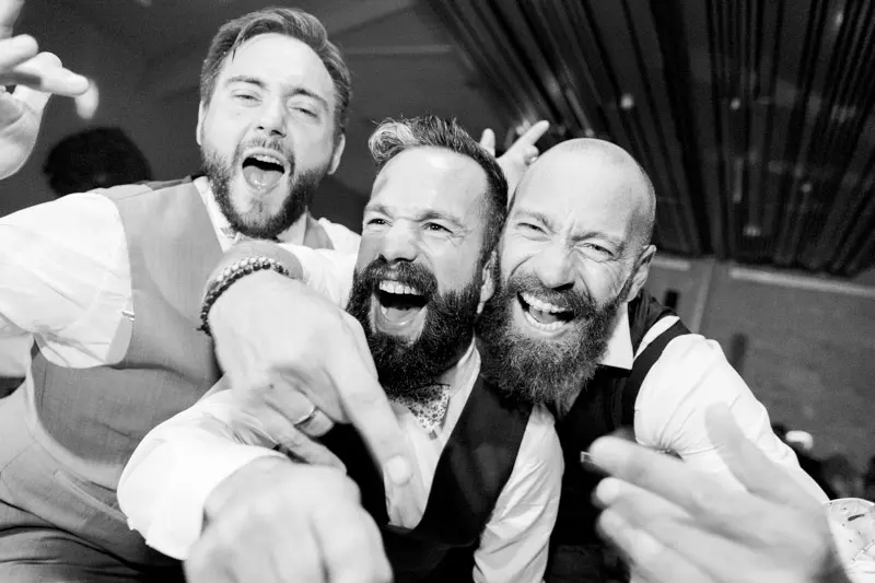 The groom and his friends roaring with laughter on the dance floor, black and white