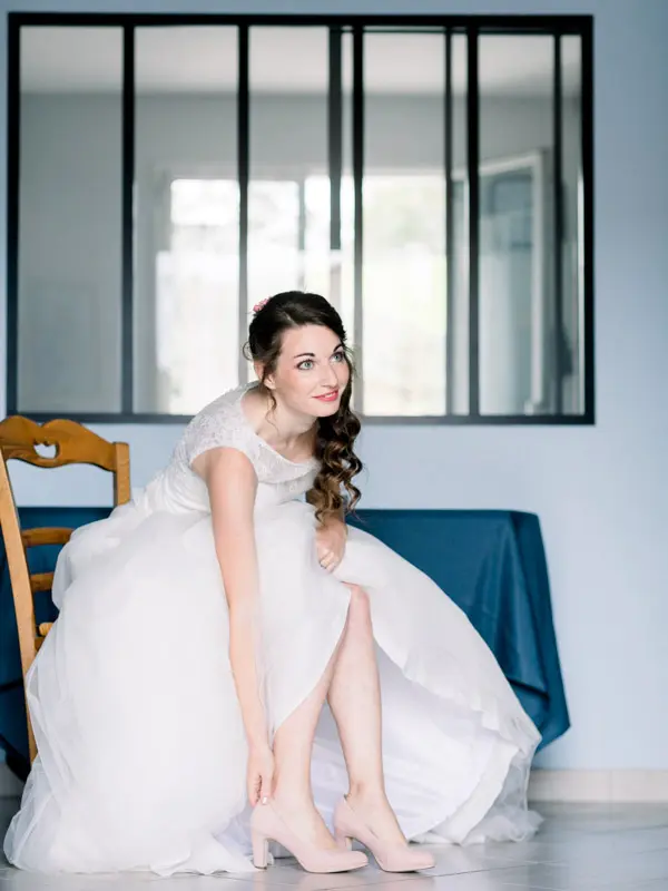 Bride sitting by a glass-panelled partition putting on her shoes