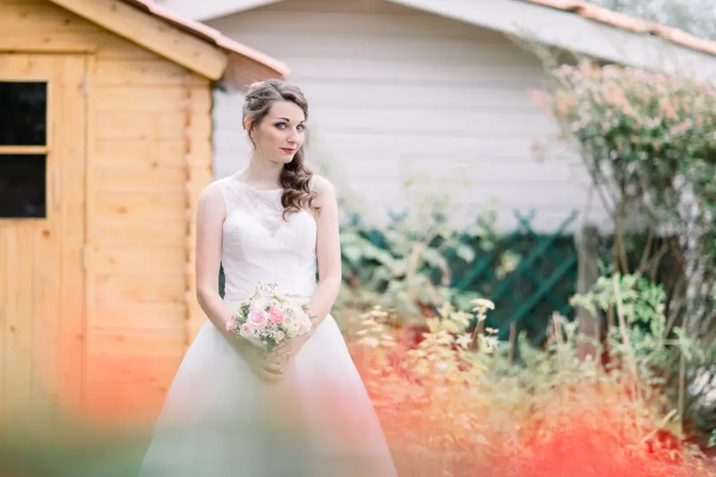 Bride with her bouquet in front of a wooden garden shed among flowers