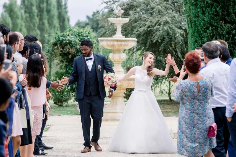 Bride and groom hand in hand passing through the guests by a fountain