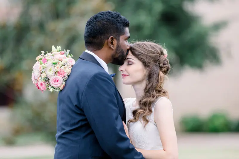 Groom kissing the bride's forehead, bouquet over his shoulder