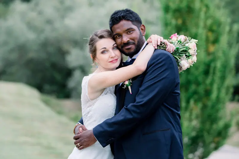 Smiling bride nestled in the groom's arms in the grounds