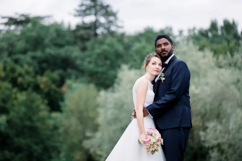 Bride leaning against the groom in front of the park's trees