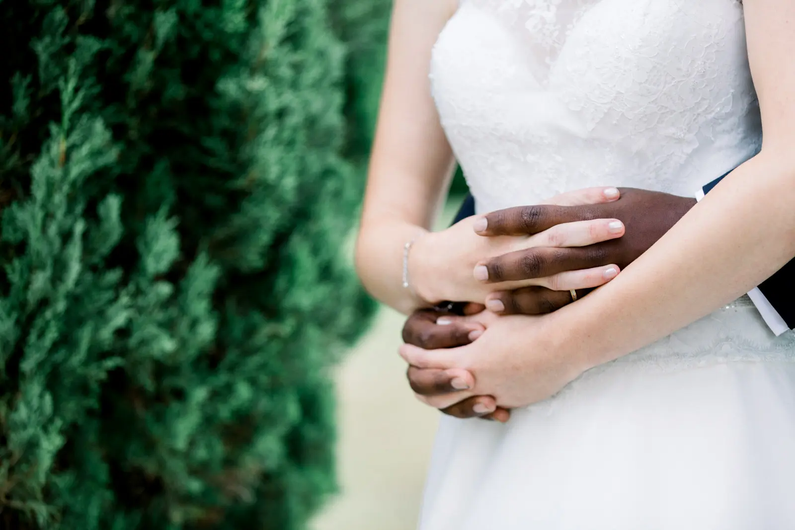 Bride and groom's hands entwined over the bride's lace gown