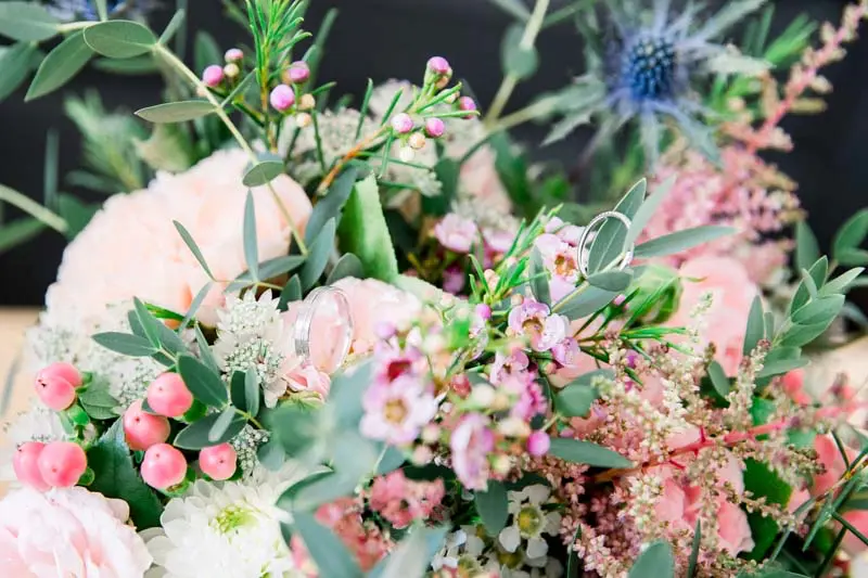 Bridal bouquet of pale roses and blue thistles with the wedding rings on top
