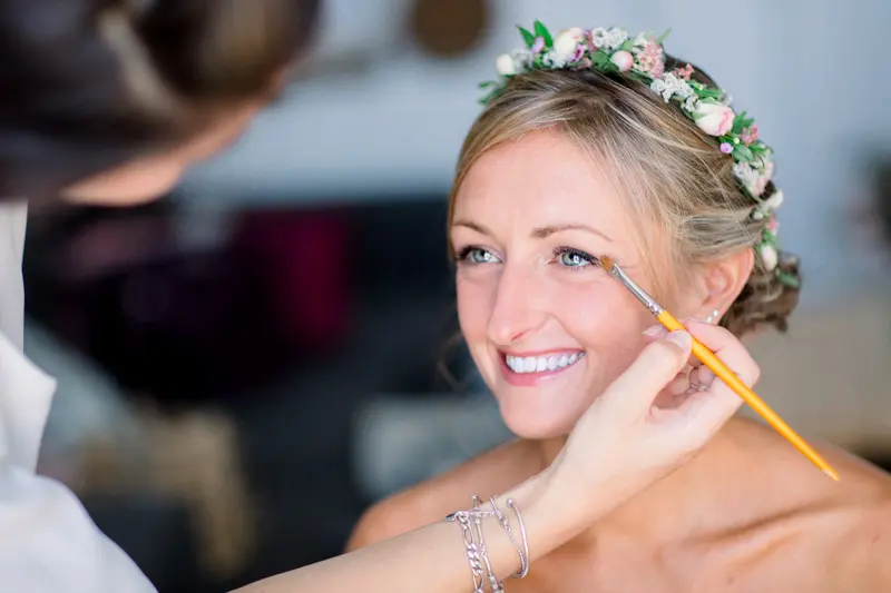 The bride smiling as her make-up is done, flower crown in her hair