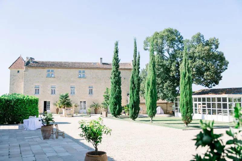 Stone façade and cypresses of Château Isabeau de Naujan under a blue sky