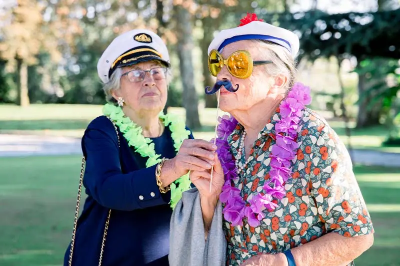 Two older guests laughing in captain's hats with photo booth props