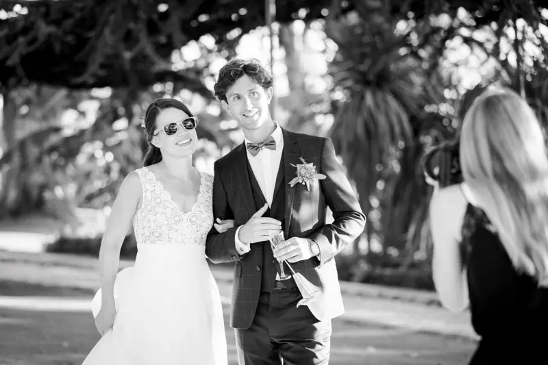 The newlyweds in sunglasses arriving arm in arm, in black and white