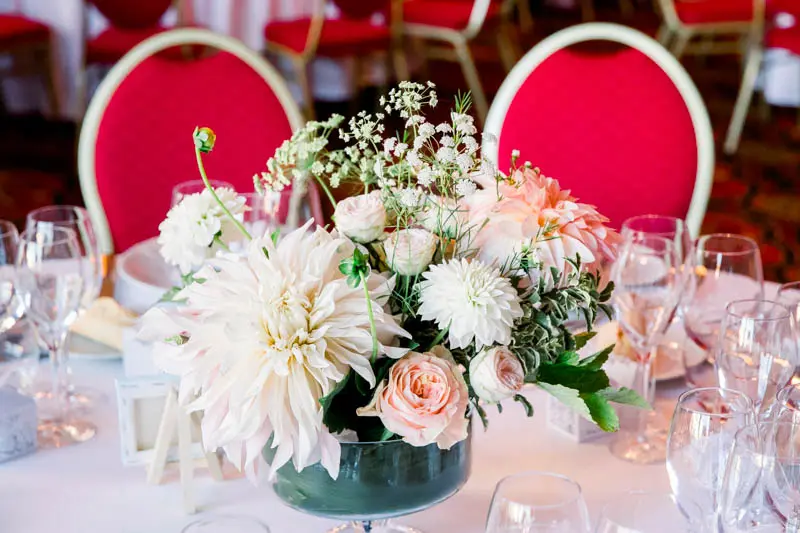 Centrepiece of dahlias and pale roses in front of red chairs