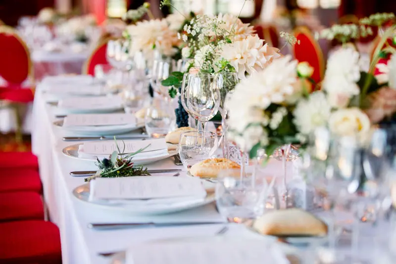 Long wedding table dressed with white flowers and red chairs