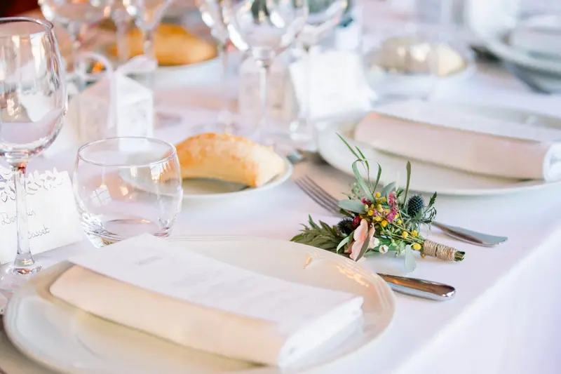 Place setting with menu, bread roll and a sprig of flowers on a white tablecloth