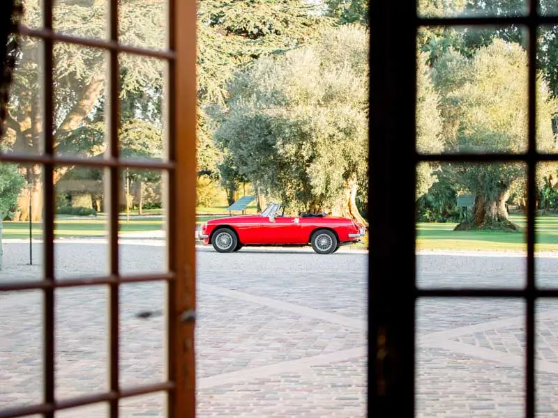 The newlyweds in a red convertible seen through a château French window