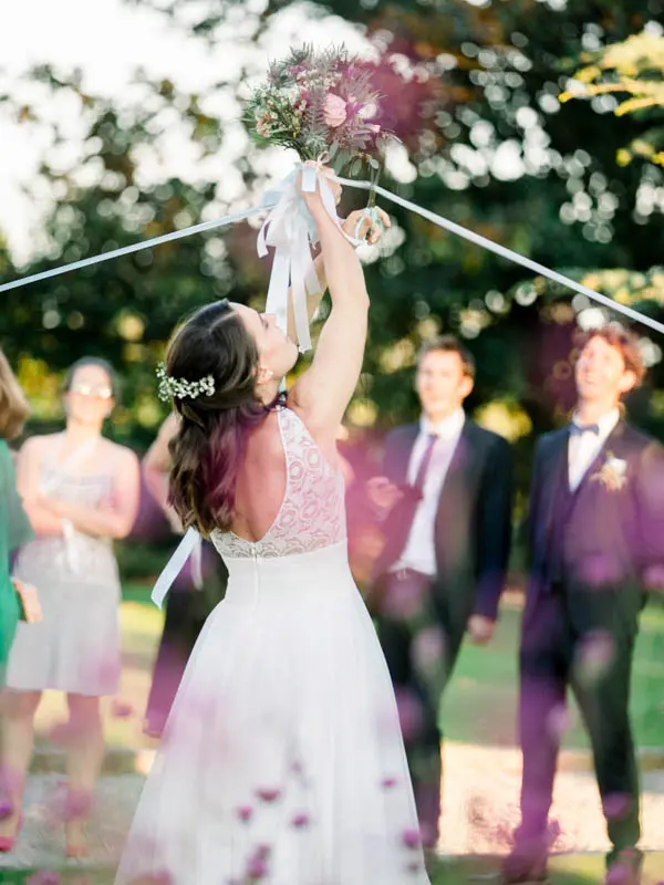 The bride raising the bouquet tied to the guests' ribbons in the park