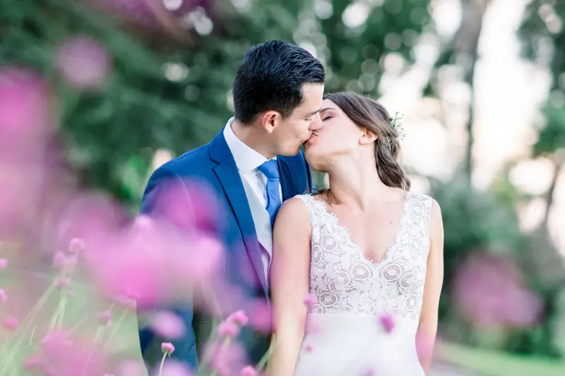 Bride and groom kissing behind pink flowers in the foreground