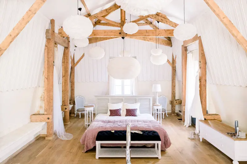 Bedroom under exposed wooden beams with white pendant lamps at Château de Garde