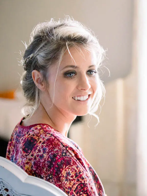 The bride with a braided updo smiling as she gets ready