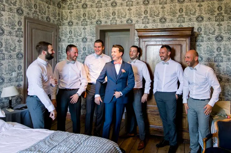 Groom and his friends in shirts in a bedroom with vintage wallpaper