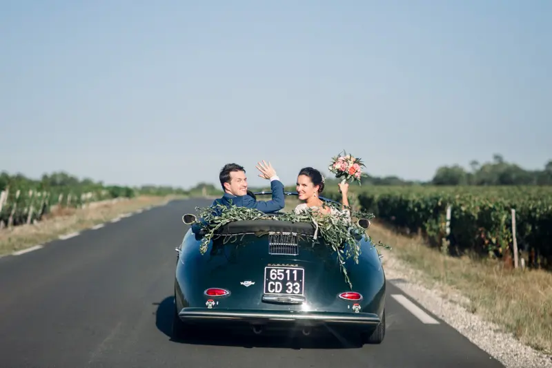 Bride and groom in a vintage Porsche convertible on a Médoc vineyard road