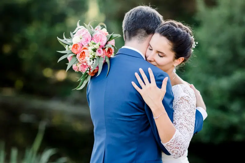 Bride and groom embracing, rose bouquet resting on the groom's shoulder