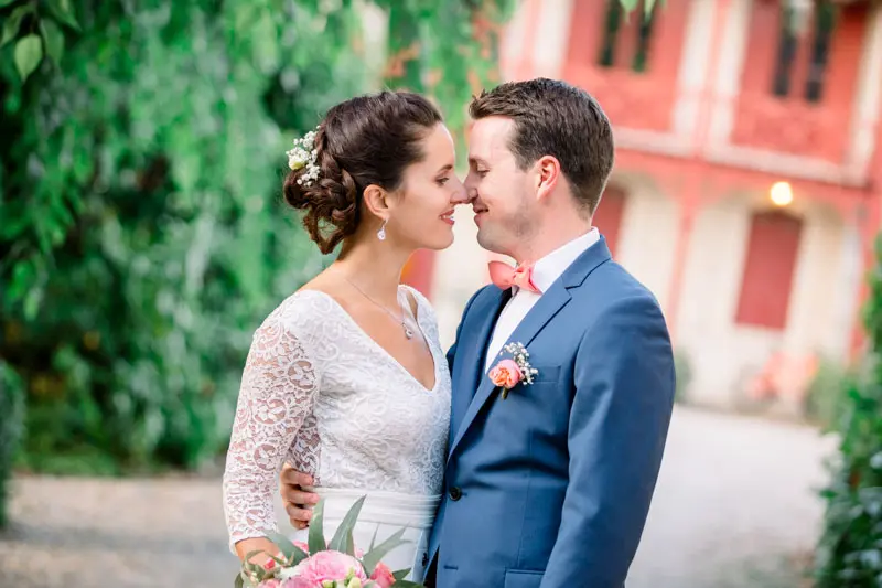 Bride and groom nose to nose in front of the pink walls of Ferme Suzanne