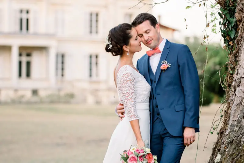 Bride and groom embracing against a tree trunk in front of the château