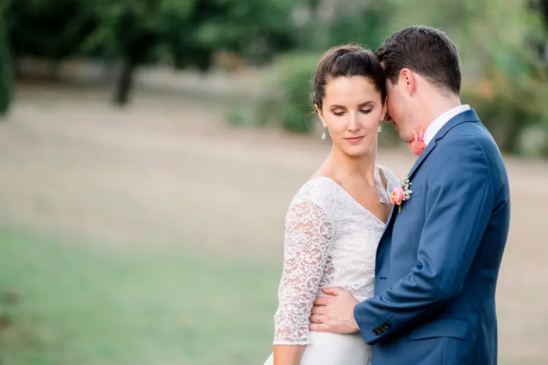 Bride and groom nestled together at the edge of the park, eyes lowered