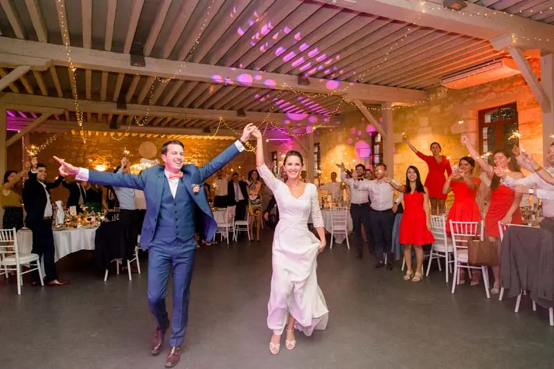 Bride and groom making their entrance arms raised in the Ferme Suzanne hall