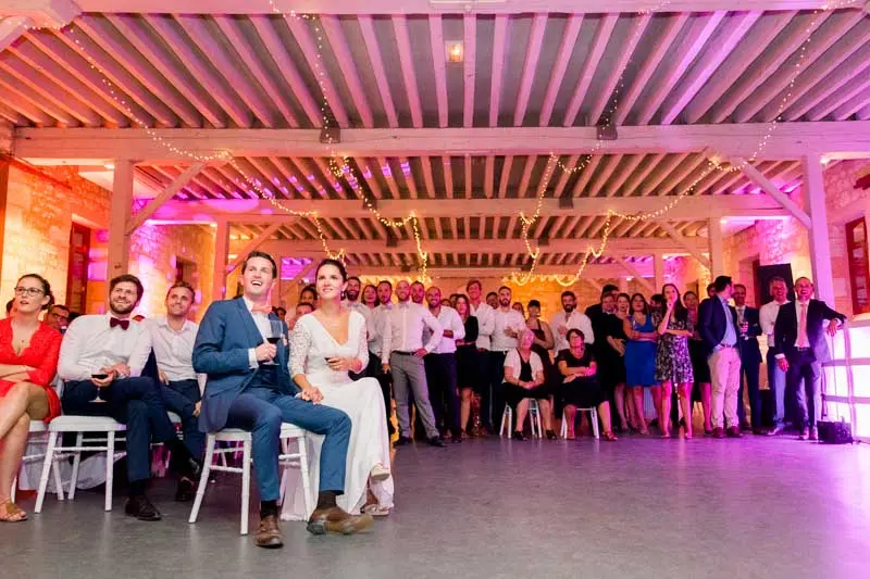 Bride and groom seated listening to speeches under the hall's pink lights