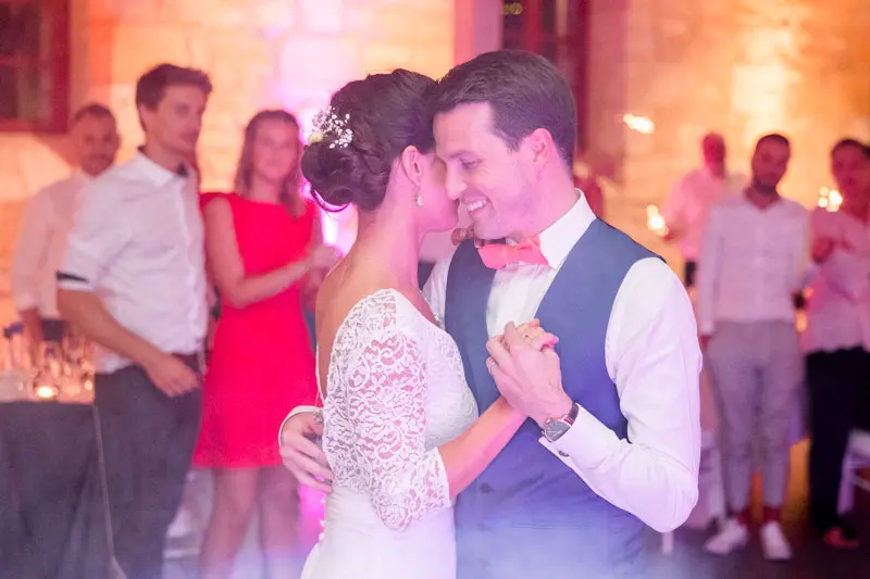 Bride and groom dancing cheek to cheek surrounded by their guests