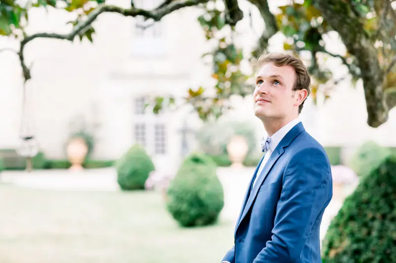 Groom in a blue suit gazing into the distance in the château garden