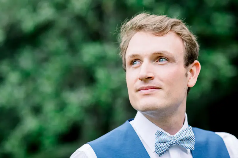 Portrait of the groom in a blue waistcoat and bow tie against greenery