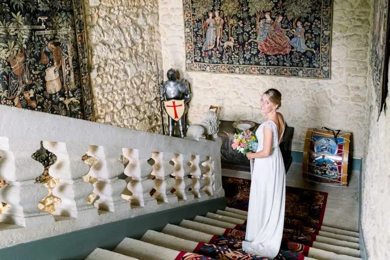Bride walking down the château's stone staircase lined with tapestries