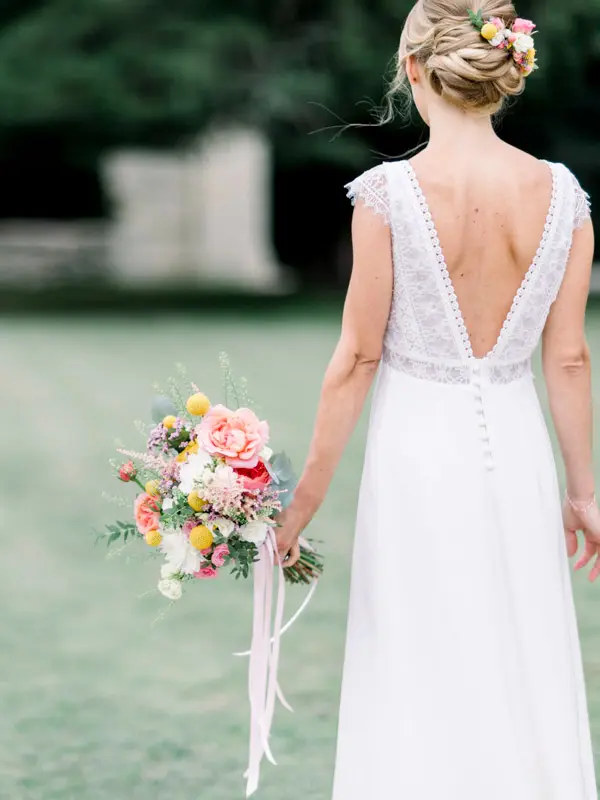 Bride seen from behind, lace-back gown and colourful bouquet in hand