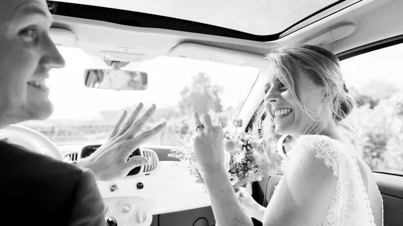 Bride and groom laughing in the open-top car, black and white