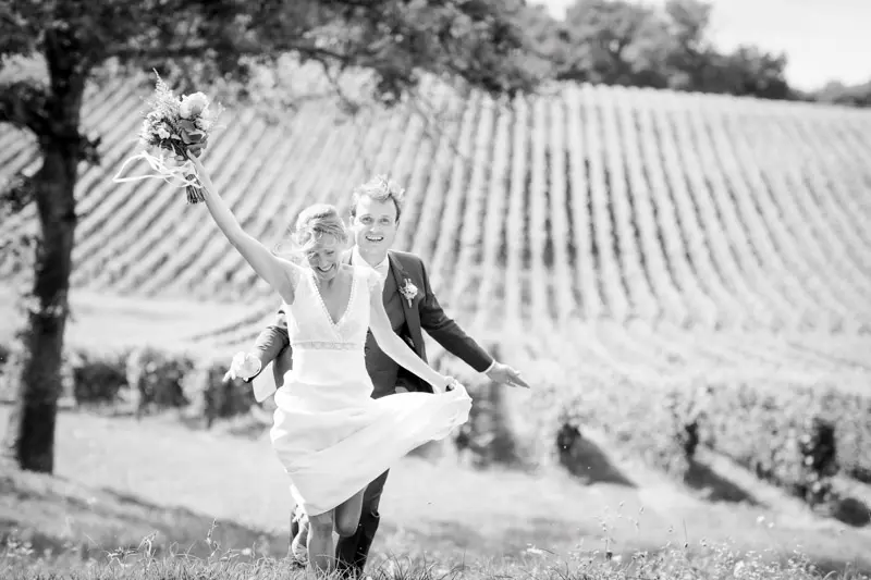 Bride running with her bouquet raised before the vines, black and white