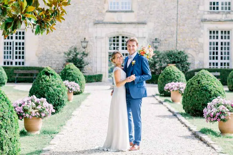 Bride and groom on the flower-lined path to the château facade