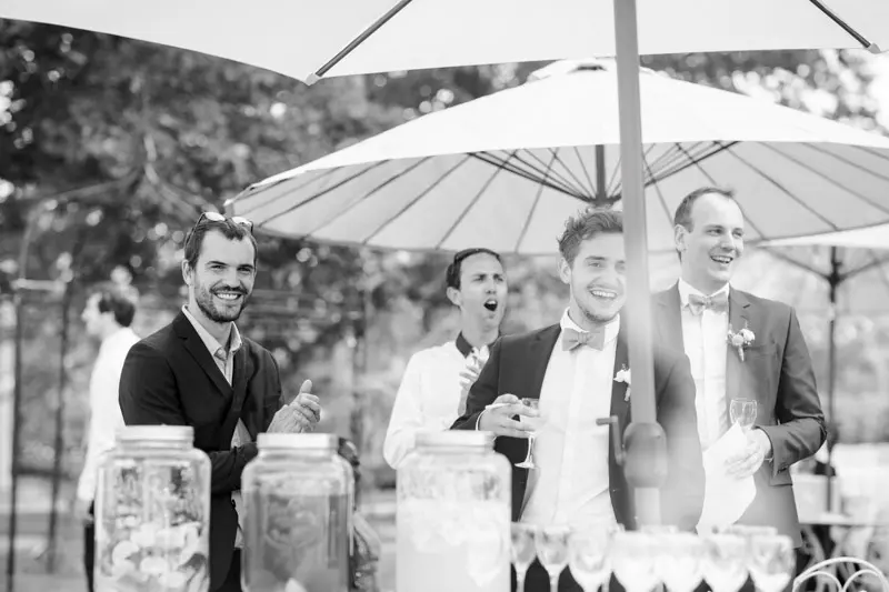 Guests in suits laughing under parasols at the cocktail hour, black and white