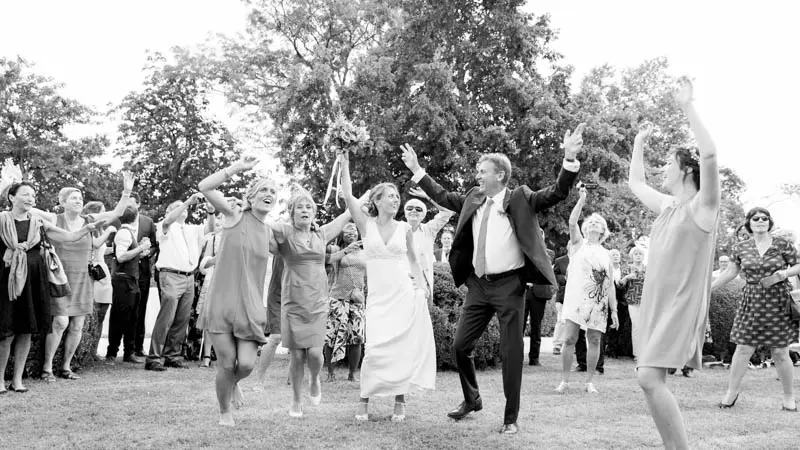 Bride, groom and guests dancing with arms raised on the lawn