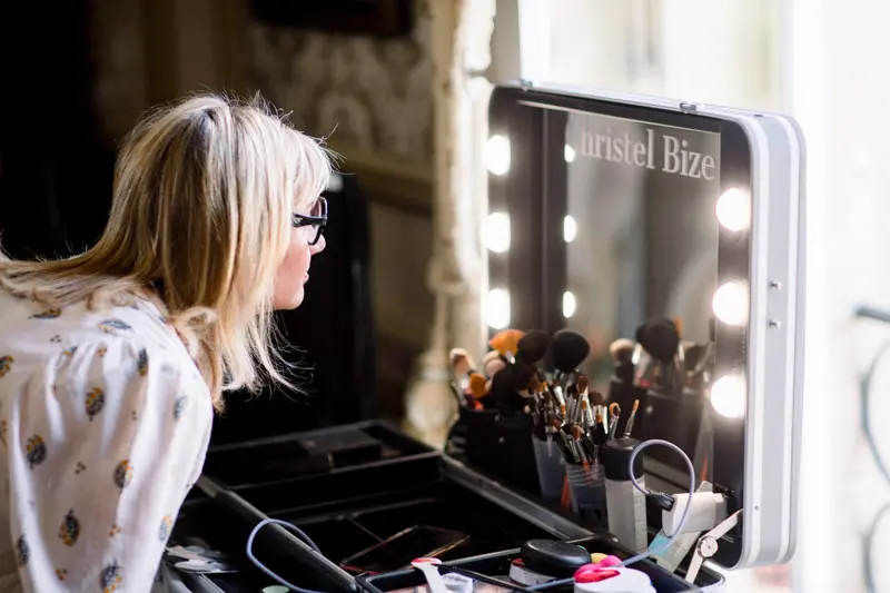 Bride facing the make-up artist's lighted mirror while getting ready