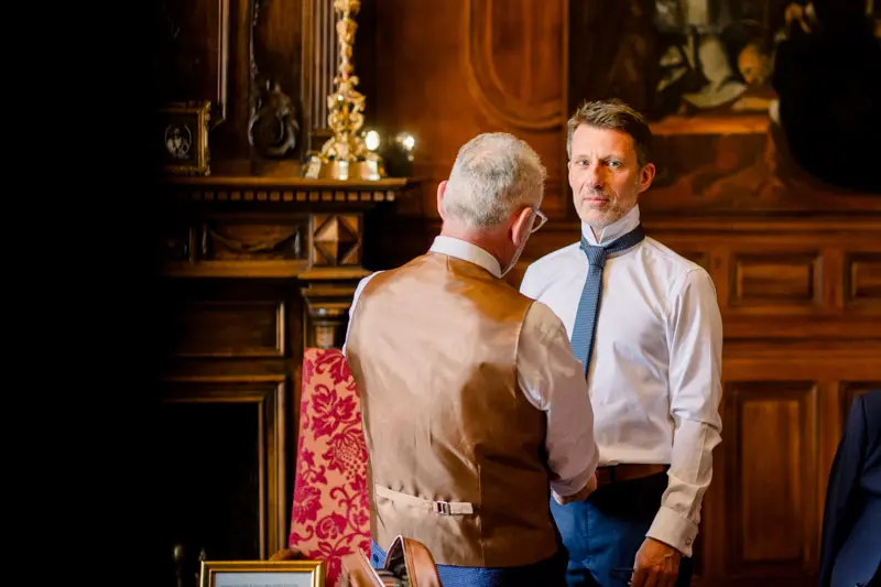 Groom and a relative getting ready in a wood-panelled château room