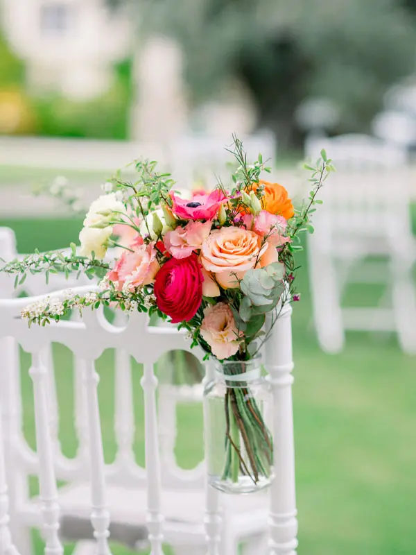 Colourful flowers in a glass jar hung on a white ceremony chair